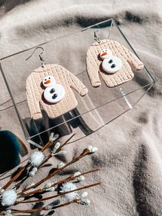 two snowmen wearing sweaters and hats are hanging from ear hooks on a clear acrylic display