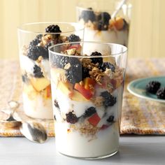 three glasses filled with fruit and yogurt on top of a table next to a plate