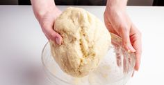 a person is kneading dough into a glass bowl on a white countertop