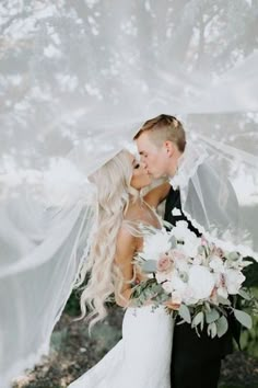 a bride and groom kissing under a veil with flowers in the foreground on their wedding day