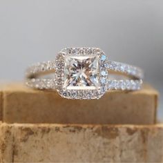 an engagement ring with a princess cut diamond surrounded by pave diamonds on top of a wooden block