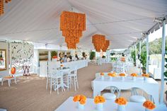 tables and chairs are set up in a tent with orange flowers hanging from the ceiling