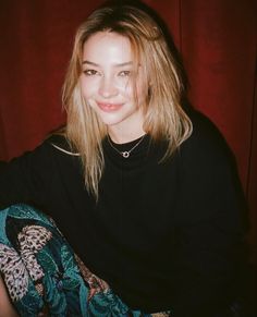 a woman sitting in front of a red curtain with her hair pulled back and wearing a black shirt