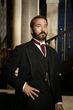 a man wearing a suit and tie standing in front of some stairs with his hands on his hips