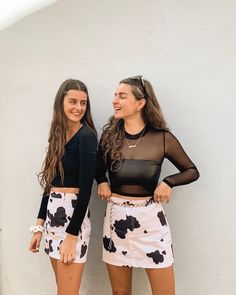 two young women standing next to each other in front of a white wall and smiling