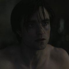 a shirtless young man stares into the distance in a dark room with only his chest visible