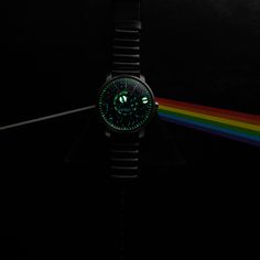 a watch with a dark side of the moon on it's face is shown in front of a rainbow - colored background