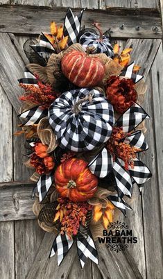 a wreath with pumpkins and plaid ribbon hanging on a wooden door, ready to be decorated for fall