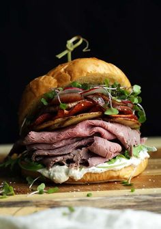 a sandwich with meat, lettuce and other ingredients on a wooden cutting board