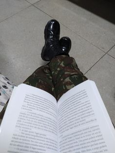 a person in camouflage pants and black shoes is reading a book on the floor with their legs crossed