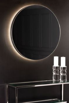 a round mirror on the wall above a console table with candles in front of it