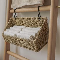 a wicker basket with towels hanging from it on a wooden ladder next to a towel rack