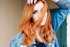 a woman with red hair is standing near a wall and holding her hand on her head