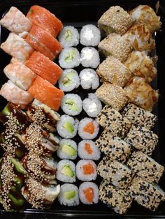 an assortment of sushi is displayed in a black tray with white rice and sesame seeds