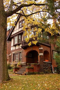 an old house with fall leaves on the ground and trees in front of it,