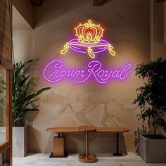 a neon crown royal sign on the side of a wall next to a bench and potted plant