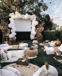 an outdoor movie party with white balloons and pillows on the grass in front of a large screen