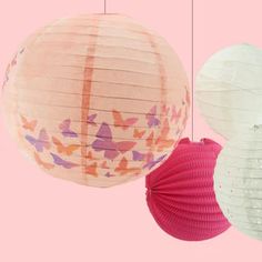 three paper lanterns hanging from strings on a pink background