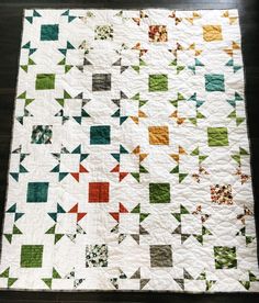 a white quilt with green, orange and red squares on it sitting on a wooden floor