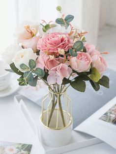 a vase filled with pink and white flowers on top of a table next to an open book