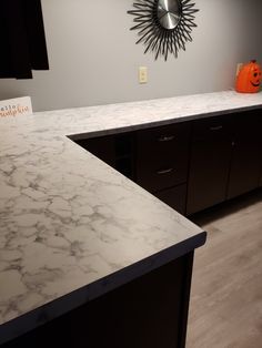 a kitchen counter top with an orange pumpkin on the wall in the background and a clock above it