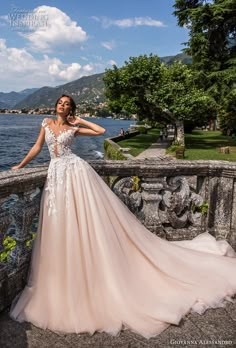 a woman in a wedding dress leaning against a stone wall near the water with her hands on her hips