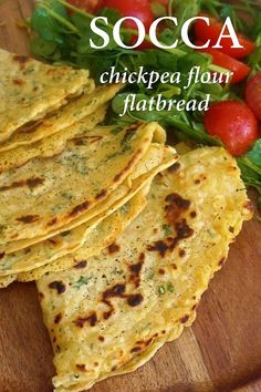 several flatbreads on a cutting board with tomatoes in the background and text that reads socca chickpea flour flatbread