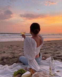 a woman sitting on top of a beach holding a glass of wine