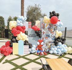 an outdoor birthday party with balloons and spiderman decorations on the lawn, along with tables and chairs