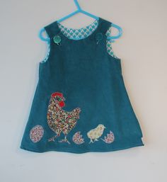 Cute  pinafore for a one to two year old. It is made from 100% cotton baby cord ie fine corduroy, which is soft and warm and is a blue green colour. The hen, chick and egg are appliqued . They are in liberty country cotton. The buttons open the neck of the pinafore for ease of putting over the head. The pinafore was created to make a n  outfit with the cotton shirts for this age .Pinafores are so versatile because they can be layered underneath if its cool with tights and t shirts or just worn with a short sleeved t if warm. My inspiration for this garment was my own grandchildren were very fond of farm animals at this age. The buttons are plastic and recycled. Looks good as an outfit with cotton retro shirts in Dotty Birds shop. Cute Cotton Sleeveless Pinafore Dress, Cute Sleeveless Cotton Pinafore Dress, Cute Sleeveless Pinafore Dress For Playtime, Cotton Dress For Easter Playtime, Cotton Easter Dress For Playtime, Casual Cotton Easter Dress, Recycled Buttons, Lion Shirt, Cute Spring