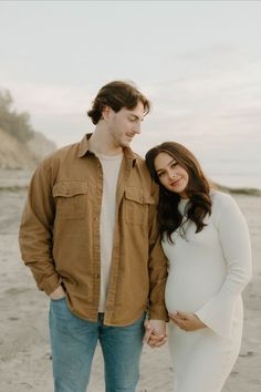 a pregnant couple holding hands on the beach