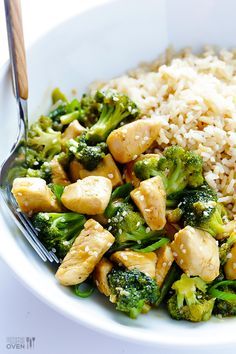 a white bowl filled with chicken and broccoli on top of rice next to a fork