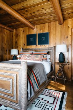 a bedroom with wooden walls and flooring has a bed in the middle, two lamps on either side