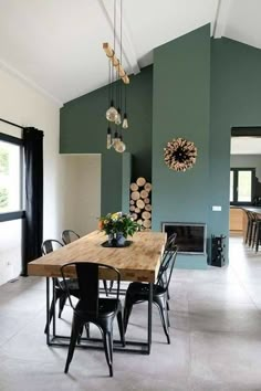 a dining room with green walls and wooden table surrounded by black chairs in front of a fireplace