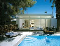 a swimming pool surrounded by palm trees next to a white house with glass walls and doors