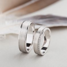 two white gold wedding bands with diamonds on them, sitting next to each other in front of a magazine