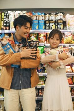 two people standing next to each other in front of a store filled with food items