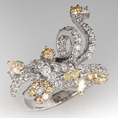 This lovely ring features a floral and ribbon design and is prong set with a total of fifty-one (51) round brilliant cut diamonds and four (4) marquise brilliant cut diamonds. The ring measures 21.1mm at the top, rises 6.4mm above the finger, tapering to 2.9mm wide and 1.2mm thick at the base of the shank. This ring is currently a size 6.5. Marquise Multi-stone Diamond Ring, Elegant Marquise Cut Multi-stone Cluster Ring, Luxury Yellow Gold Flower Ring With Diamond Accents, Luxury Yellow Gold Flower Ring In Sterling Silver, Luxury Marquise Multi-stone Diamond Ring, Luxury Multi-stone Marquise Cut Diamond Ring, Luxury Marquise Cut Multi-stone Diamond Ring, Luxury Gold Flower-shaped Diamond Ring, Luxury Multi-stone Diamond Flower Ring