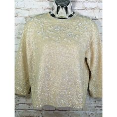 a gold top with sequins on the neck and sleeves, hanging against a brick wall