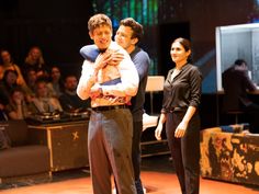 two men and a woman standing on stage with one holding the other in his arms