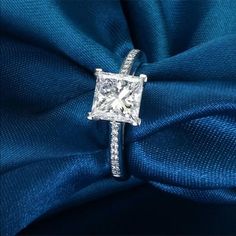 a princess cut diamond ring on top of a blue cloth