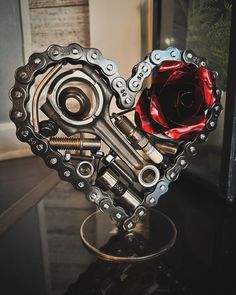 a heart shaped metal object on top of a black table with a red rose in the center