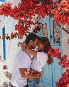 a man and woman embracing in front of a blue door with red flowers on it