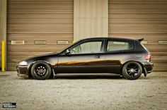 a black car parked in front of a garage door with two brown doors behind it