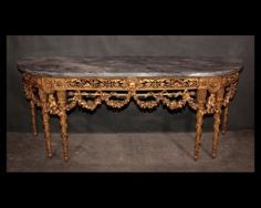 an antique console table with marble top and gold leaf decorations on the legs, in front of a black background