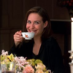 a woman sitting at a table with a cup in her hand and flowers on the table