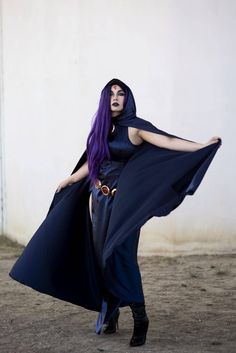 a woman with long purple hair wearing a black cape and blue dress is standing in the dirt