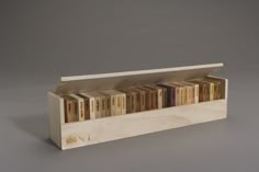 a wooden book case filled with books on top of a gray surface next to a white wall