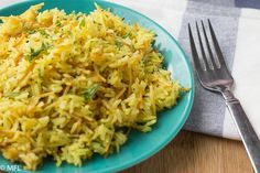 a blue plate topped with yellow rice next to a fork and napkin on top of a wooden table