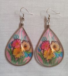 a pair of earrings with colorful designs on them sitting on a white cloth covered surface